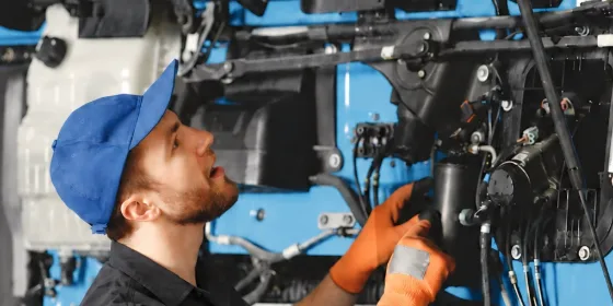 Técnico de boné azul e luvas laranja trabalhando na parte elétrica de um caminhão azul